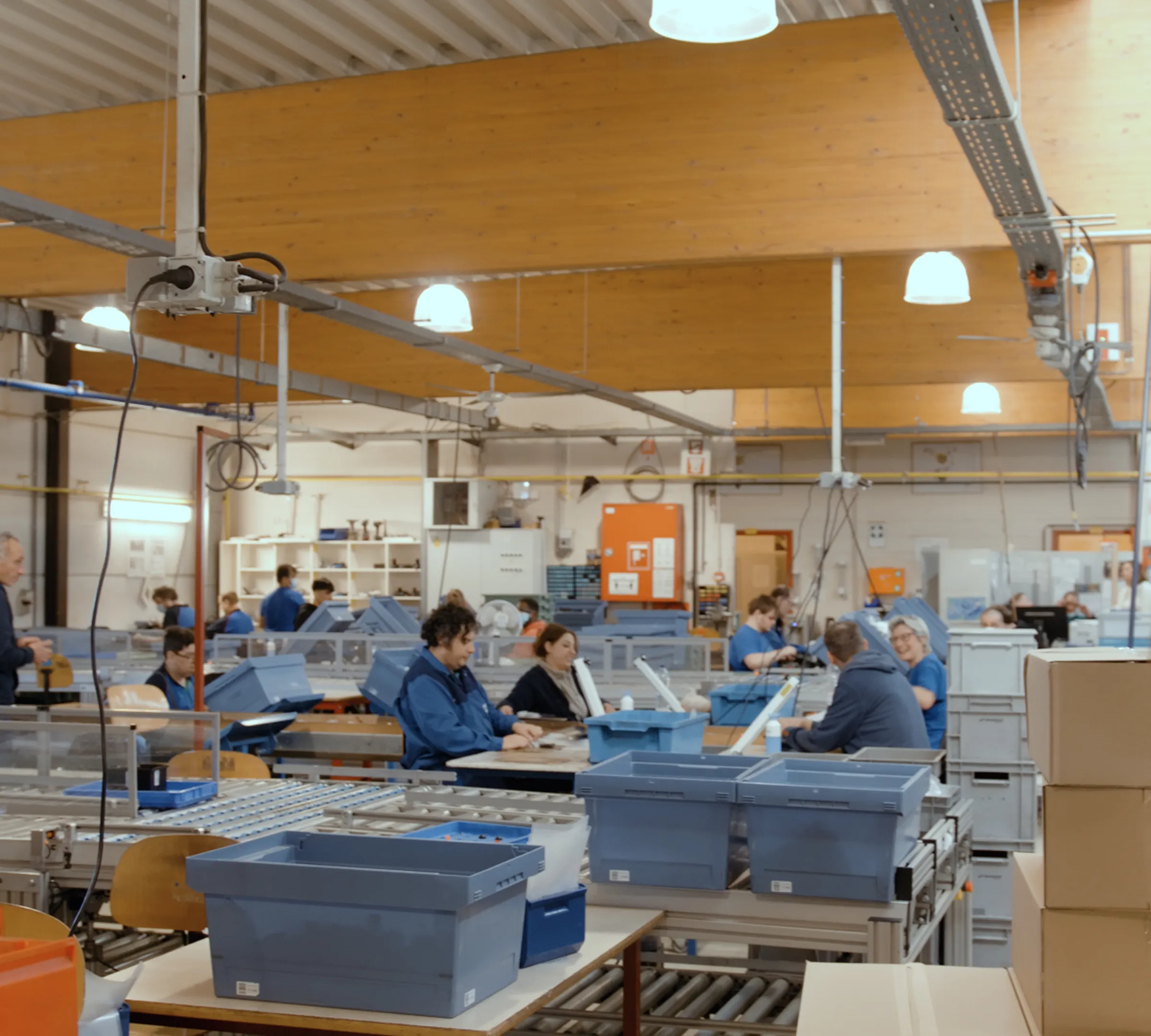 De werkvloer van Oesterbank: medewerkers in blauwe werkkledij monteren producten aan werktafels tussen bakken en rollenbanen