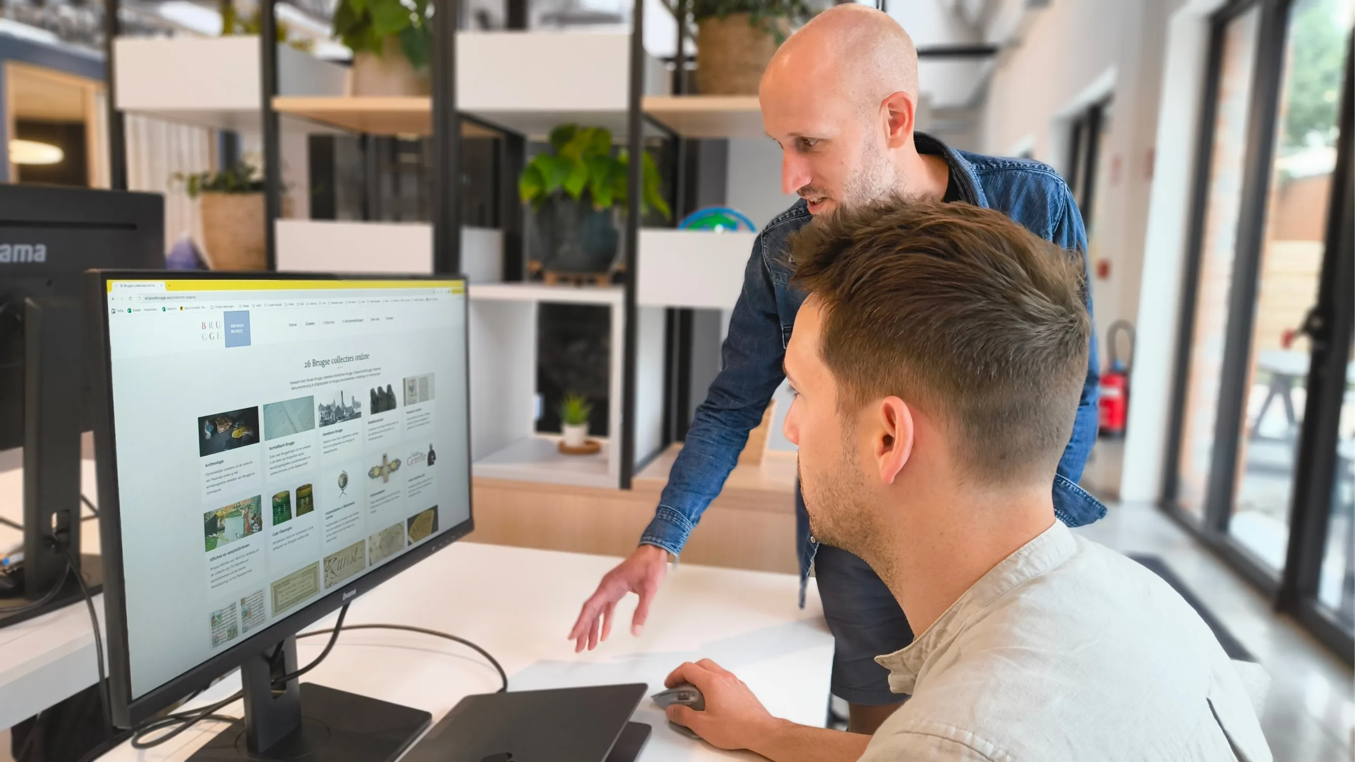 Twee collega's bekijken samen een interface op een groot scherm in het kantoor