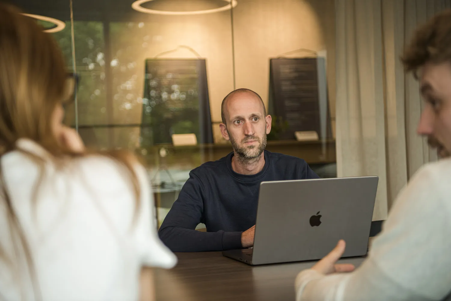 Een Octoo-collega achter zijn laptop luistert aandachtig naar twee collega's tijdens een overleg aan tafel