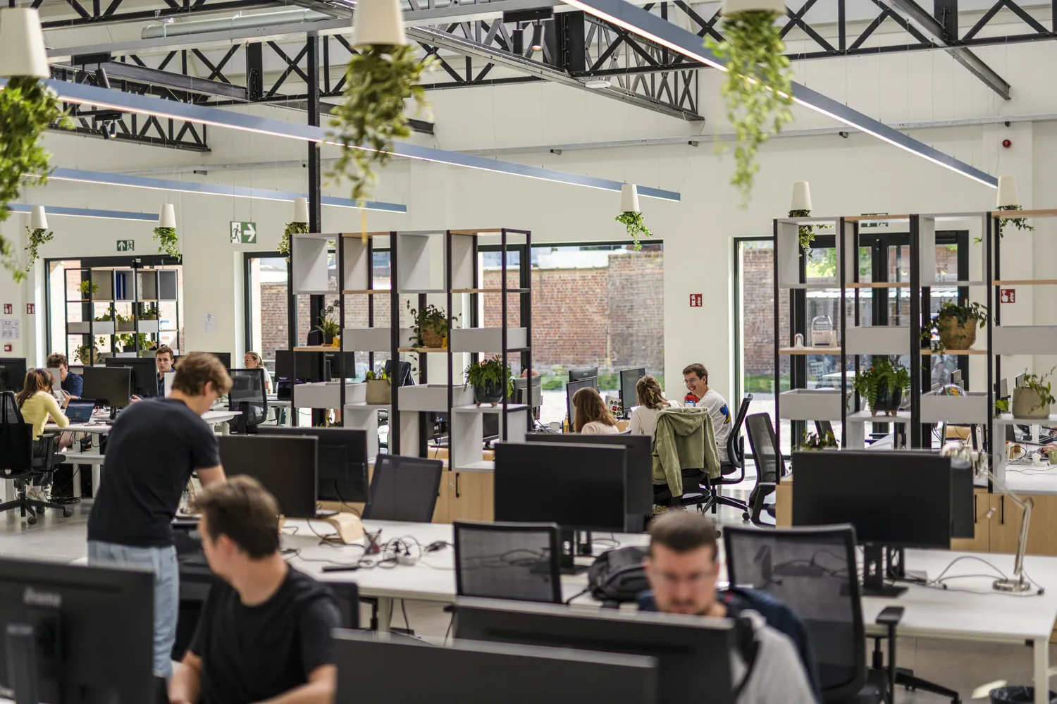 Een lichte, open kantoorruimte waar verschillende mensen aan hun bureau werken en overleggen