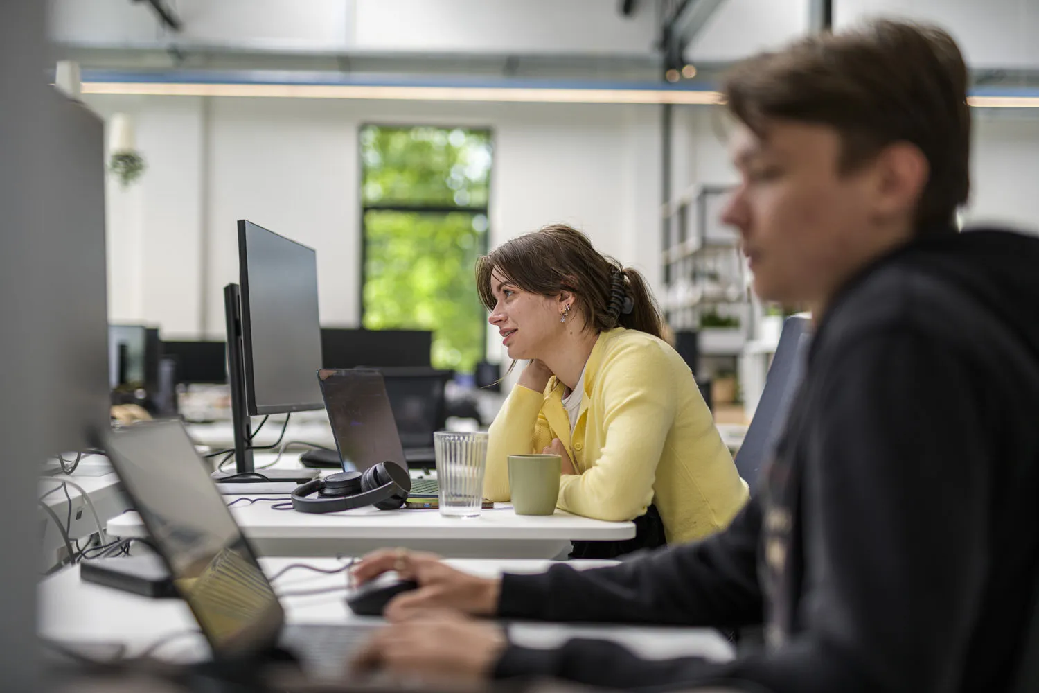 Een collega bekijkt glimlachend haar scherm terwijl een teamgenoot naast haar doorwerkt