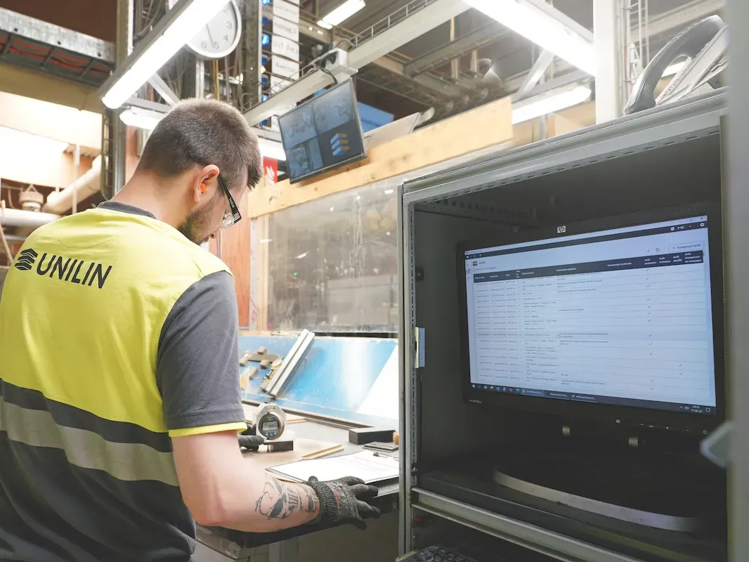 Een operator met veiligheidsbril en handschoenen werkt aan een post met de shopfloorapplicatie op het scherm